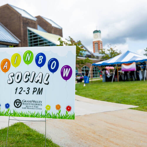 A blue and white tent outside of Kirkhof is decorated with pride flags. A yard sign reads "Rainbow Social, 12-3pm"